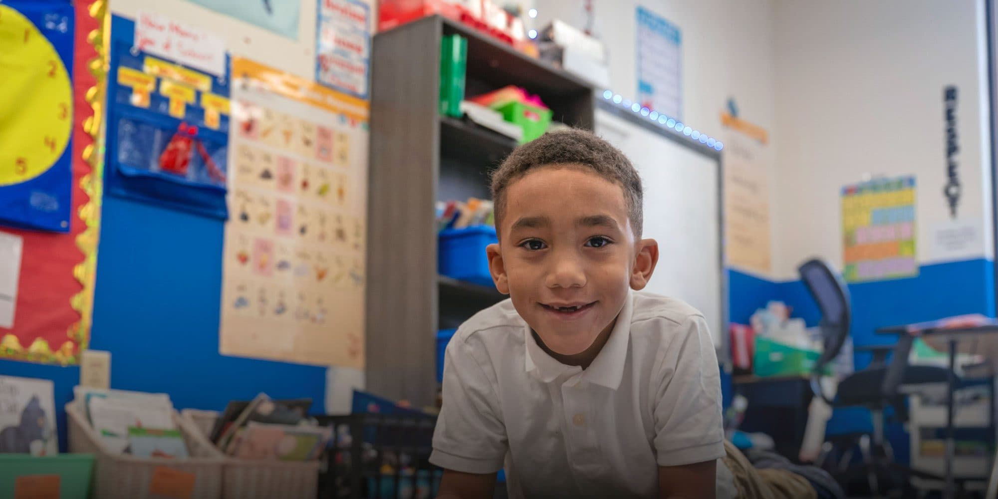 Smiling young student in a white polo shirt in a colorful classroom.